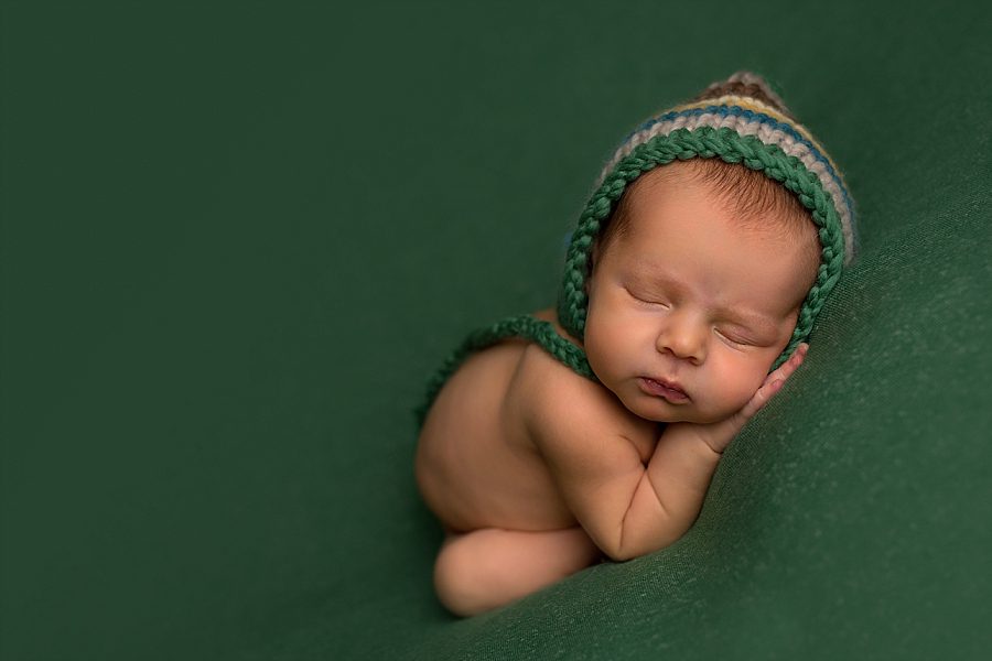 sleeping newborn on green backdrop with striped bonnet