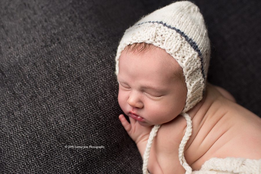 newborn portrait of baby on grey wearing white knitted pants and bonnet
